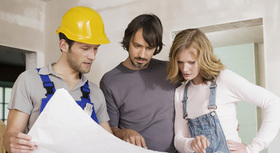 Engineer cosulting blueprints with a young couple in their new house.