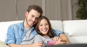Young heterosexual couple sitting on a sofa in front of a tv.
