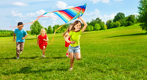 Kids running across a meadow playing with a kite.