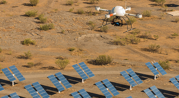 Aerial drone hovering above solar panels in a desert environment.