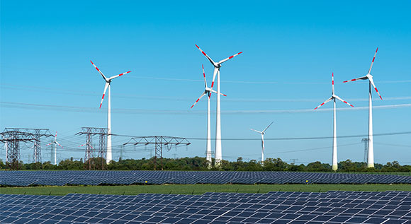 Wind turbines, solar panels and powerlines under blue sky.