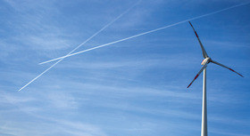 Windrad vor blauem Himmel mit Kondensstreifen