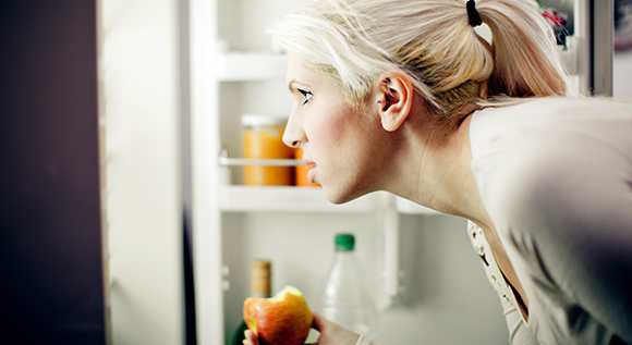 Frau schaut in einen geöffneten Kühlschrank.